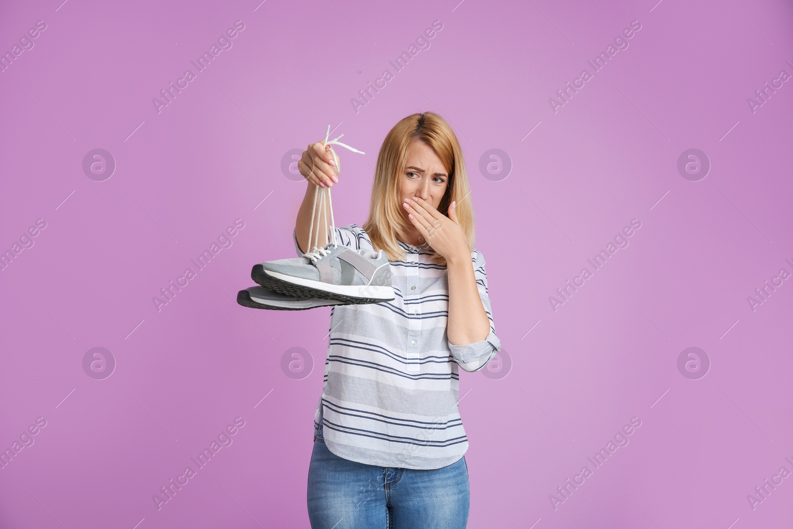 Photo of Young woman with stinky shoes on color background. Air freshener