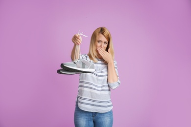 Young woman with stinky shoes on color background. Air freshener