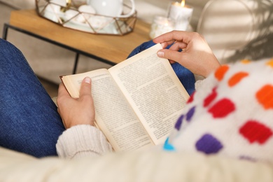 Photo of Woman wearing warm sweater reading book at home, closeup