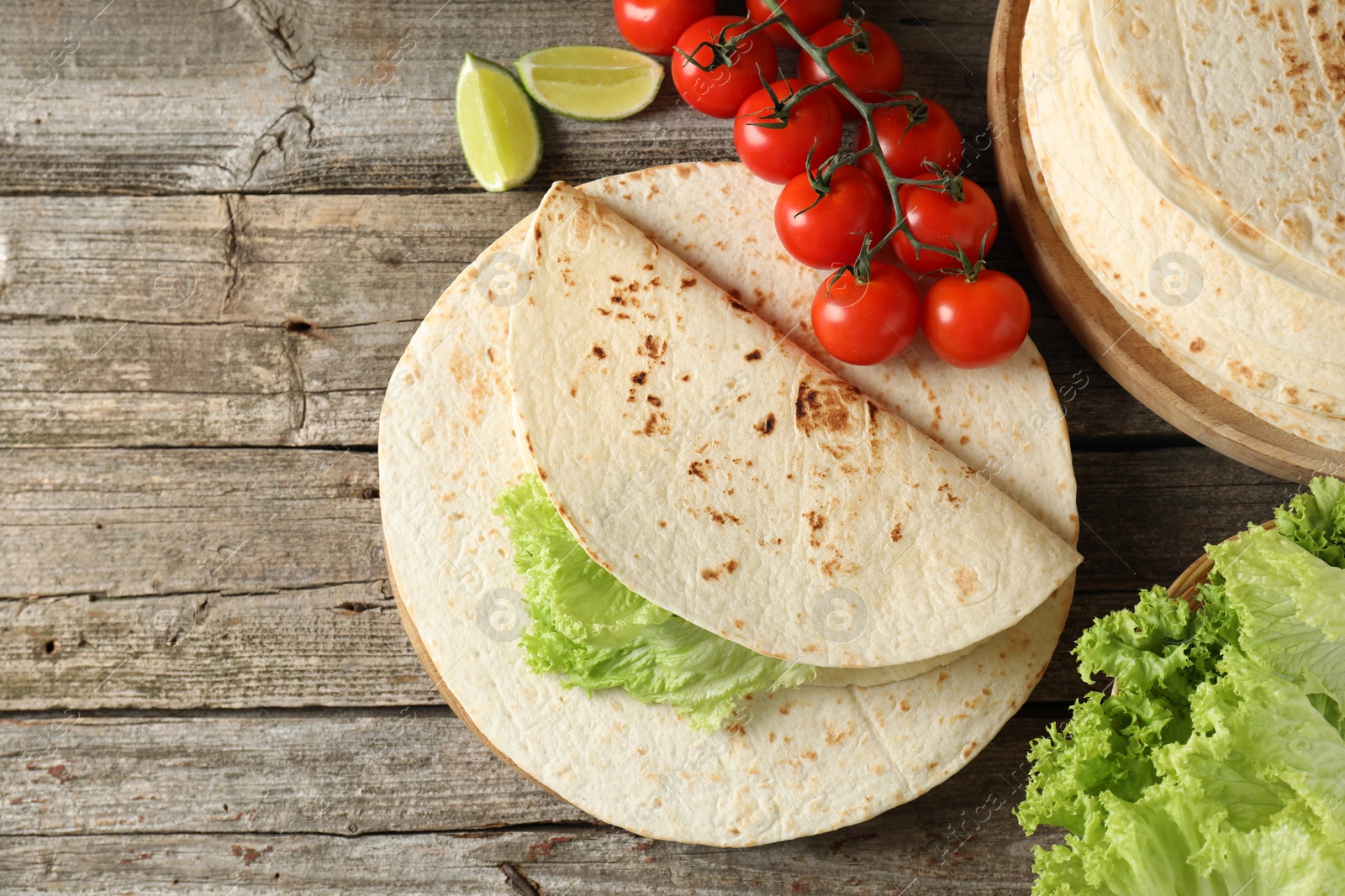Photo of Tasty homemade tortillas, tomatoes, lime and lettuce on wooden table, top view. Space for text
