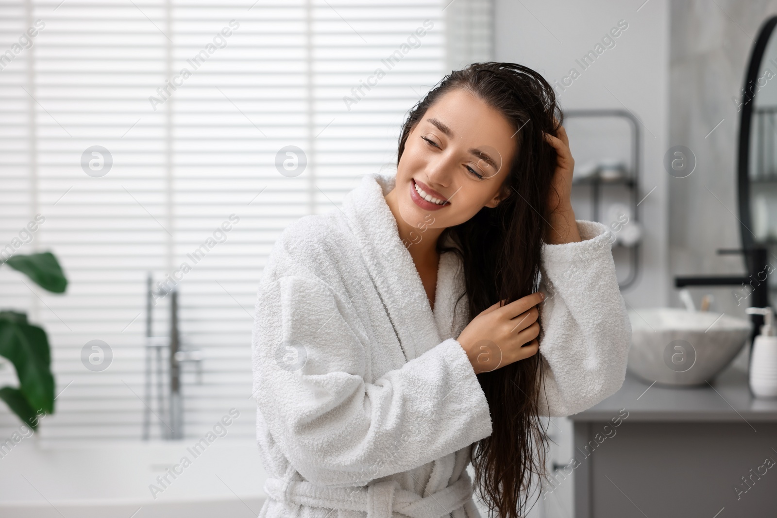 Photo of Smiling woman wearing bathrobe after shower in bathroom. Space for text