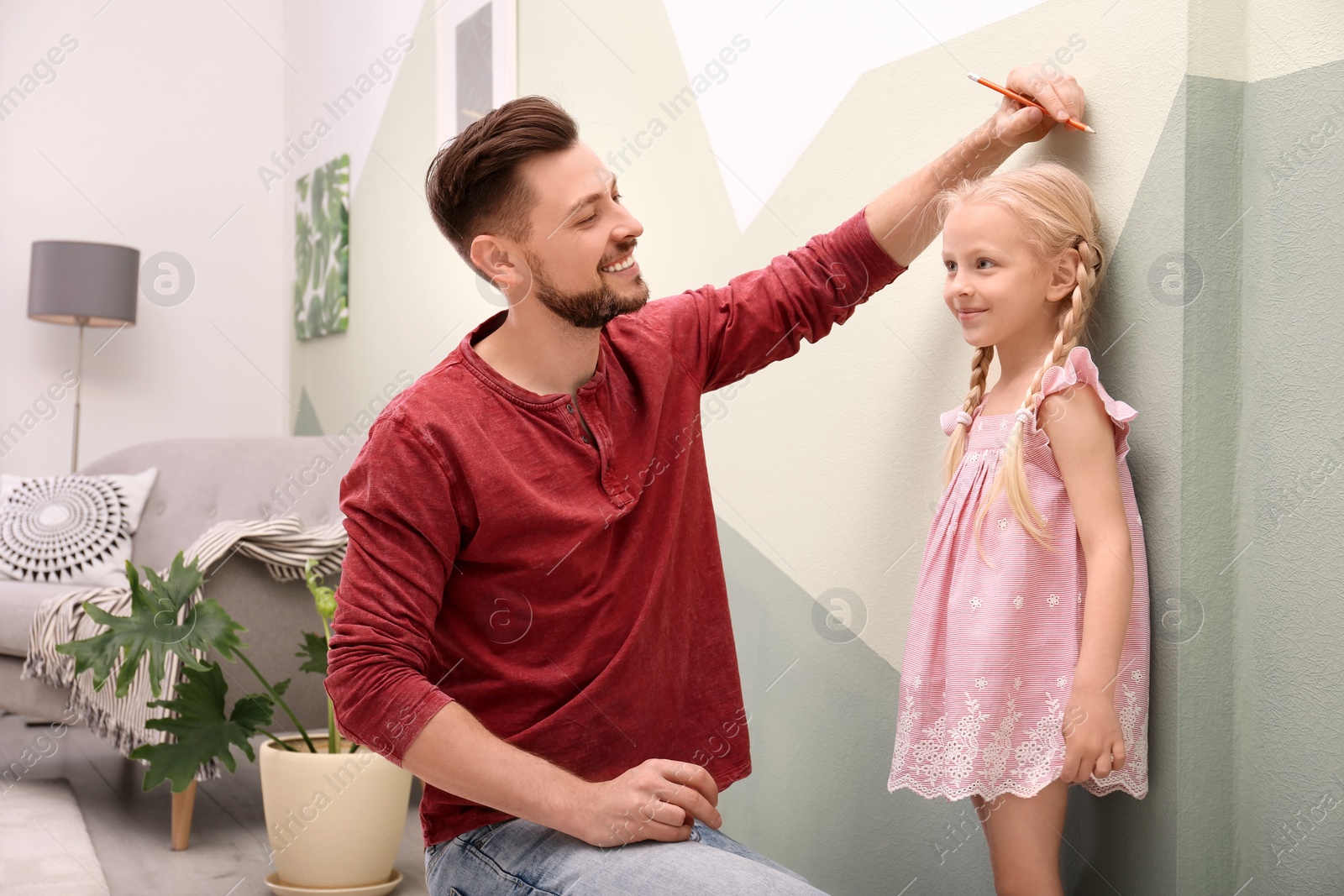 Photo of Young man measuring his daughter's height at home