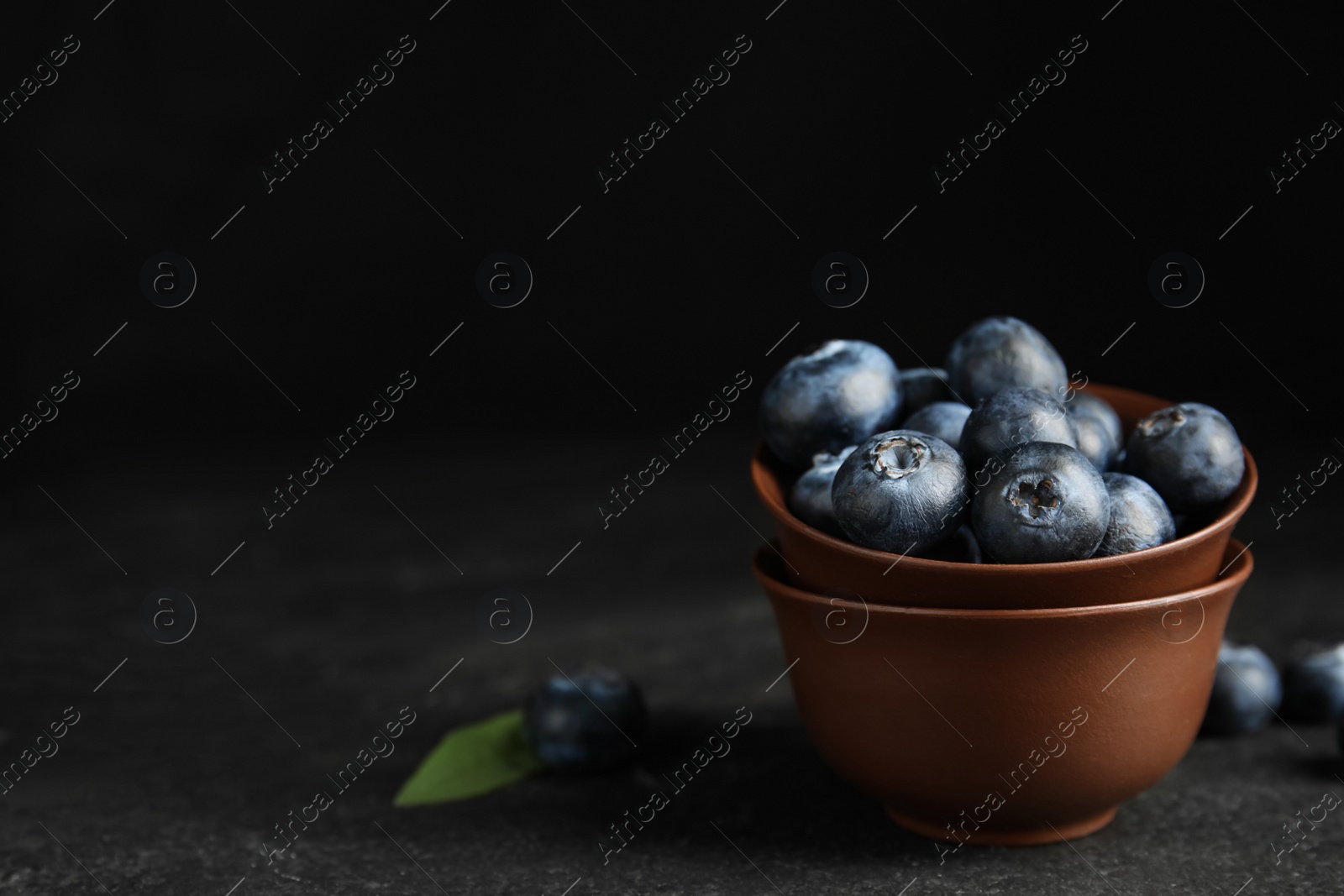 Photo of Fresh ripe blueberries in bowl on dark table. Space for text