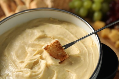 Photo of Dipping piece of bread into fondue pot with melted cheese at table, closeup