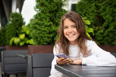 Photo of Teenage girl using smartphone at table in outdoor cafe, space for text