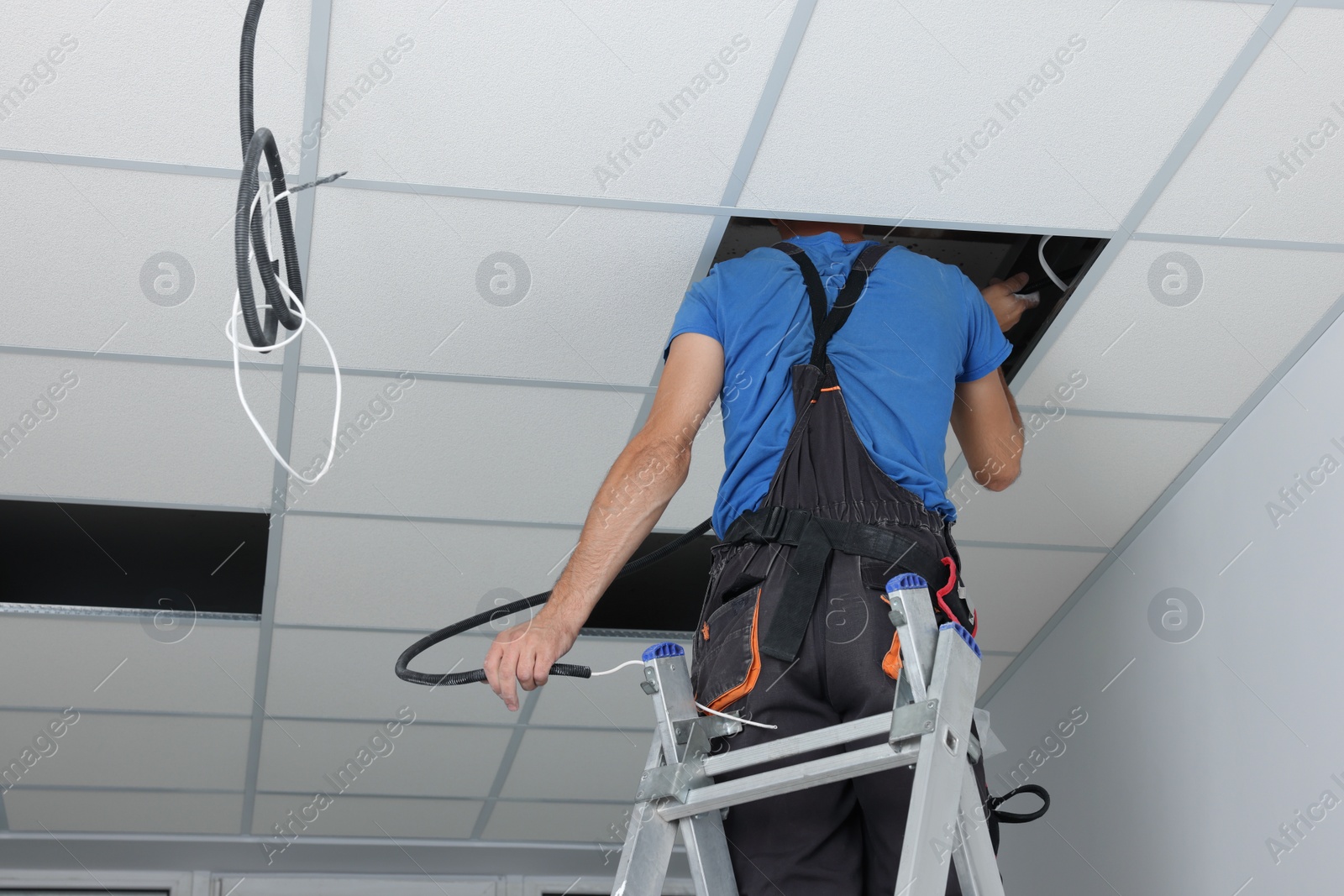 Photo of Installing ceiling lighting. Electrician working on step ladder in room