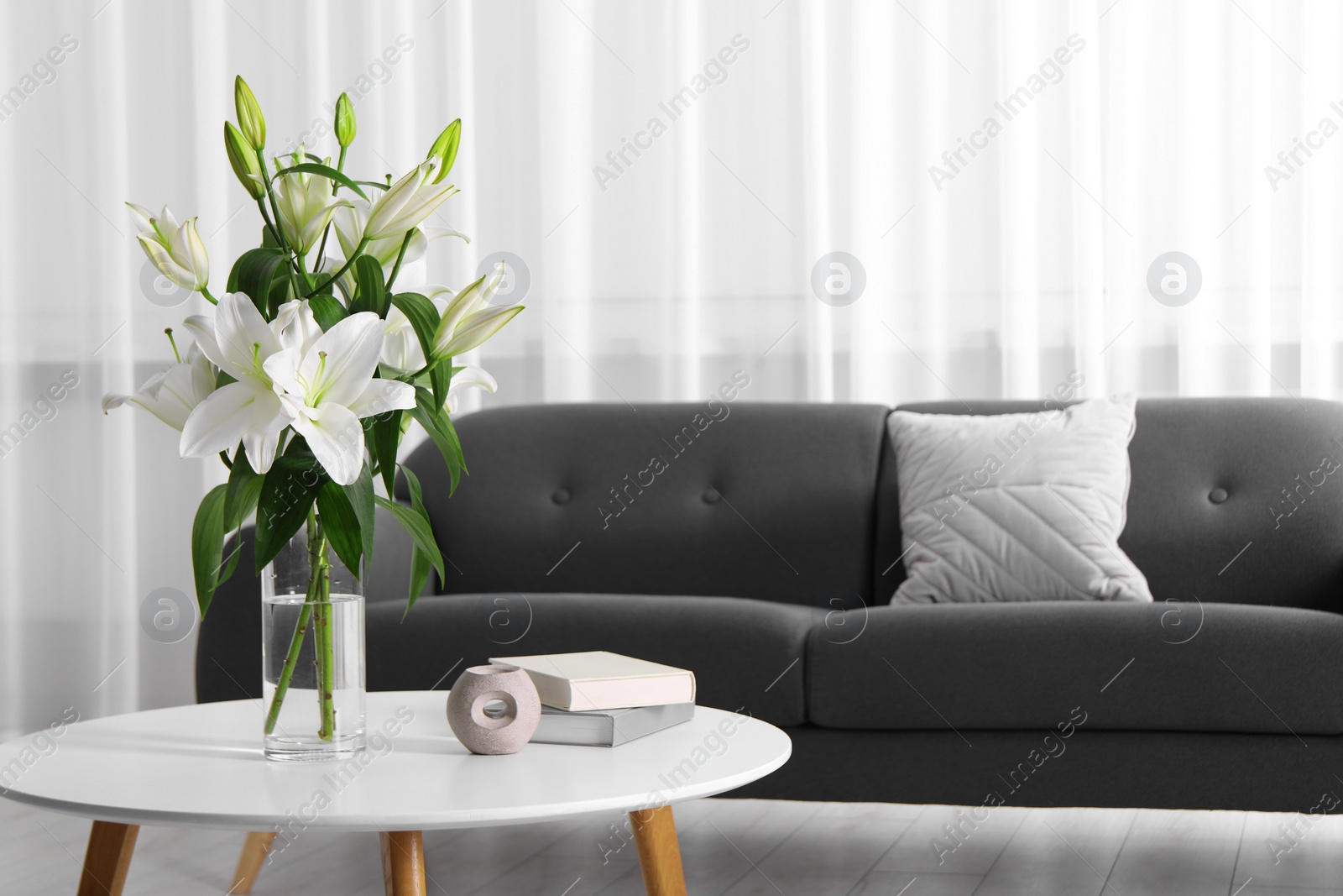 Photo of Beautiful bouquet of lily flowers in glass vase, aromalamp and books on coffee table in living room, space for text