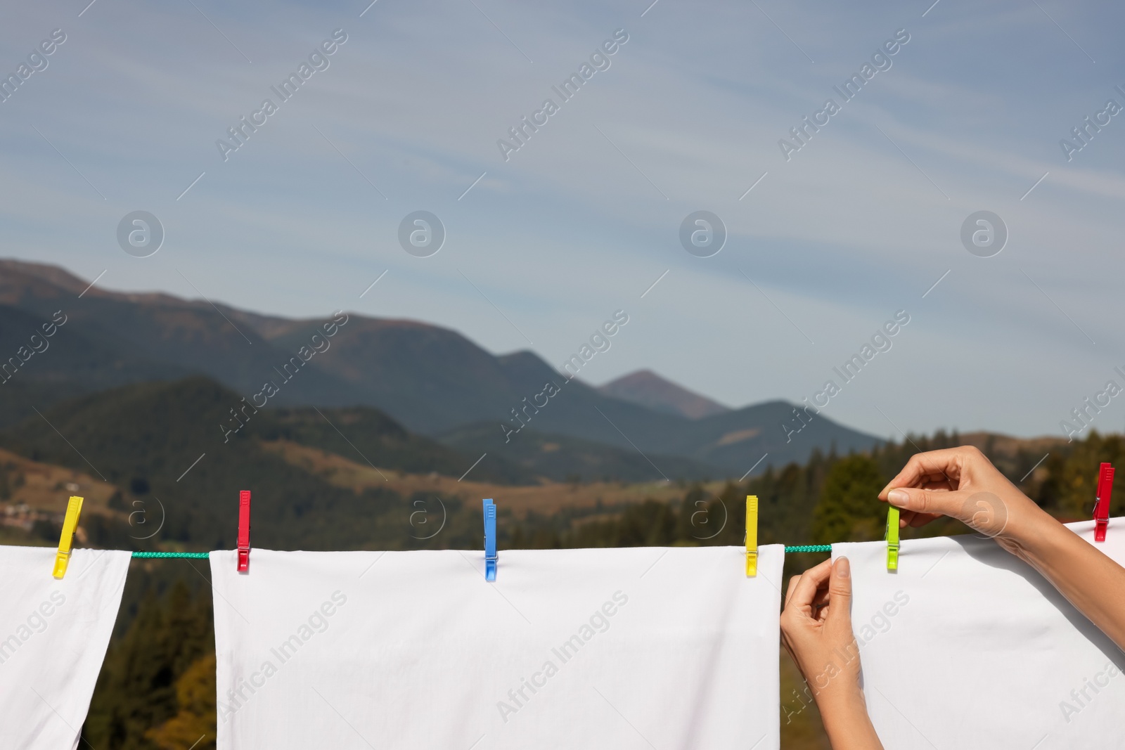Photo of Woman putting clothes pins on laundry line outdoors, closeup. Space for text