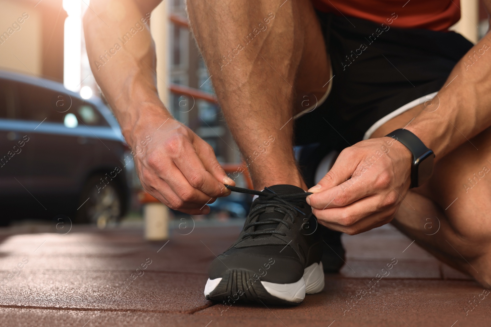 Photo of Man tying shoelaces before training at outdoor gym, closeup