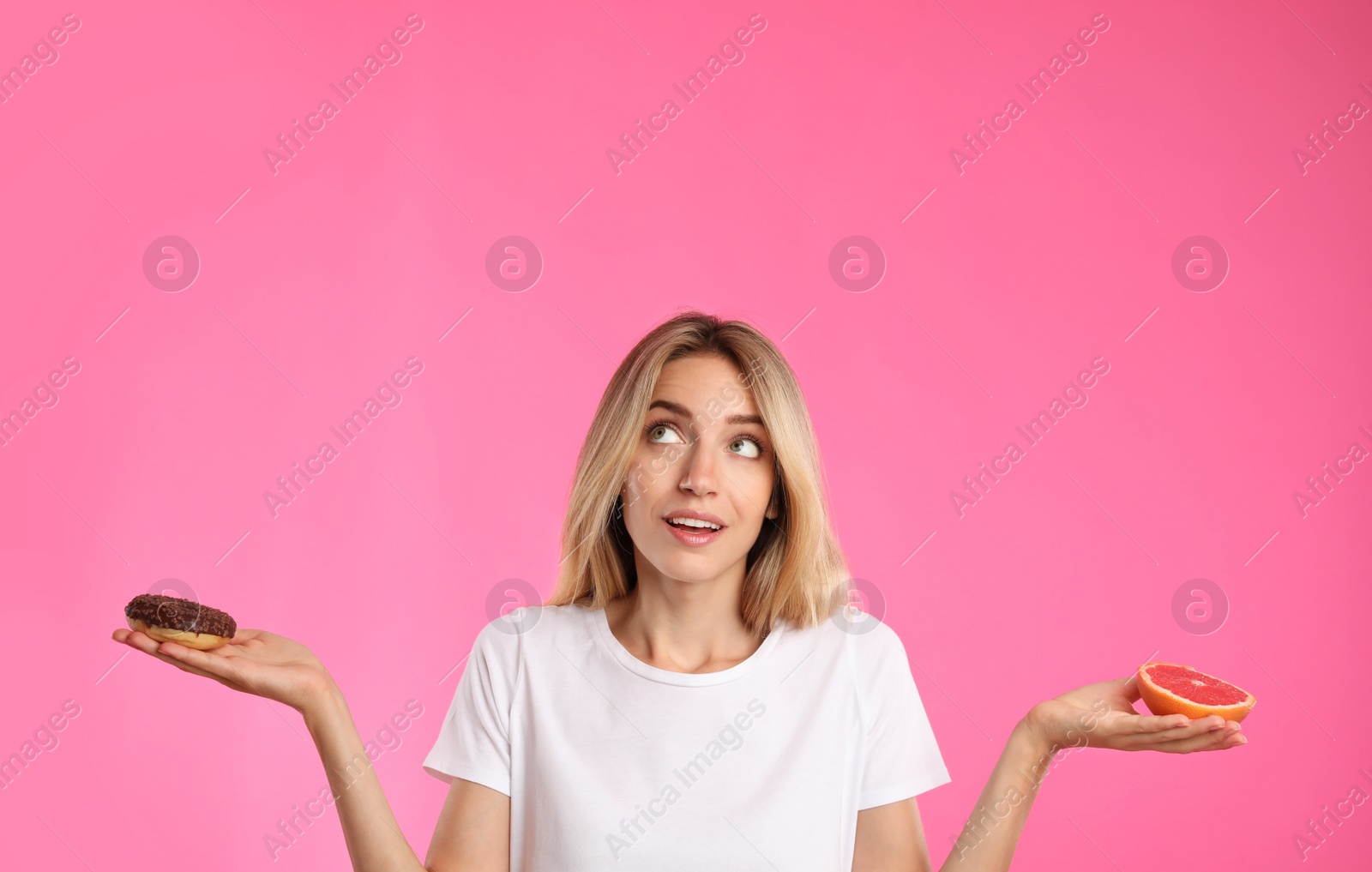 Photo of Woman choosing between doughnut and healthy grapefruit on pink background