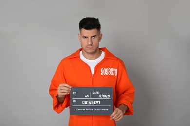 Photo of Mug shot of prisoner in orange jumpsuit with board on grey background, front view