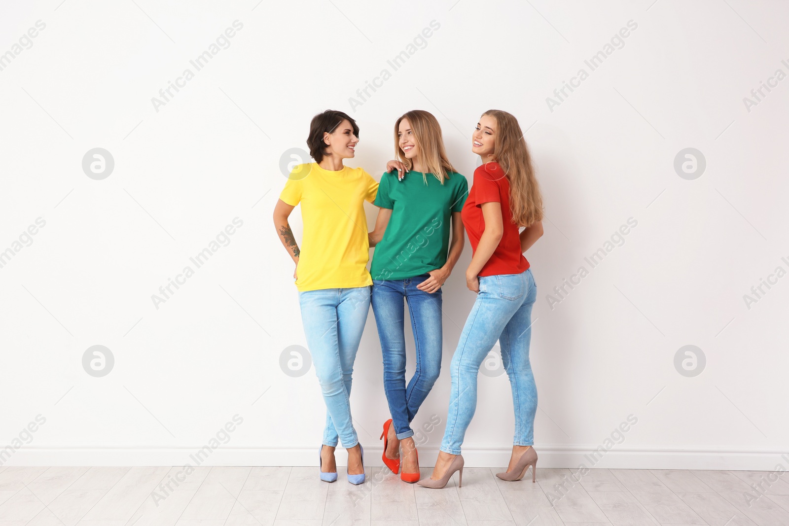 Photo of Group of young women in jeans and colorful t-shirts near light wall