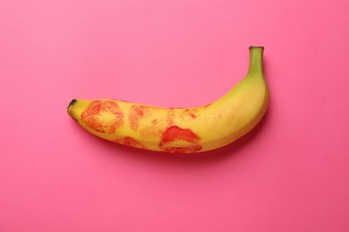 Banana with red lipstick marks on pink background, top view. Sex concept