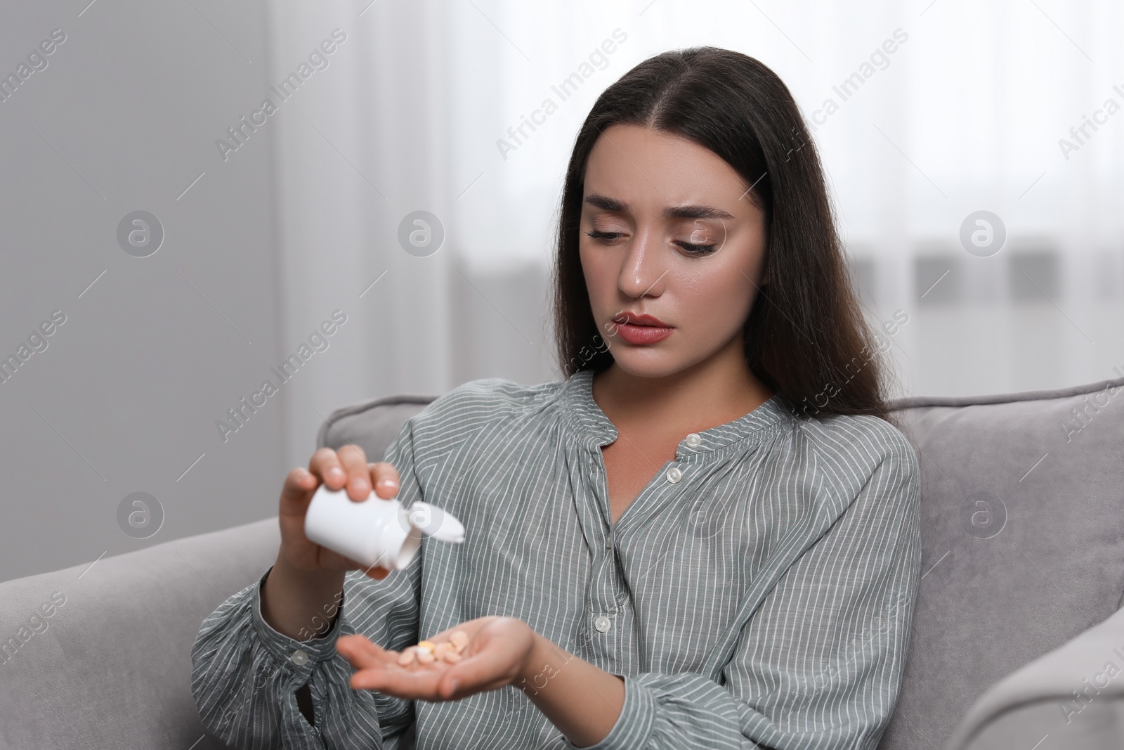 Photo of Depressed woman pouring antidepressants from bottle in armchair indoors