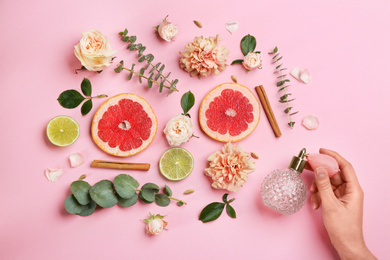 Photo of Top view of woman spraying perfume on pink background, flowers and citrus fruits representing aroma