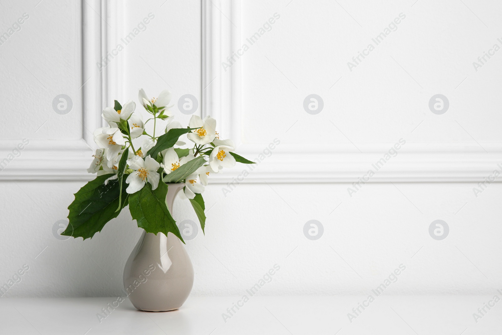 Photo of Beautiful bouquet with fresh jasmine flowers in vase on white table indoors, space for text