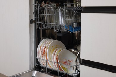 Photo of Open modern dishwasher with dirty tableware in kitchen