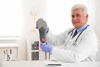 Photo of Senior male orthopedist showing insole in clinic