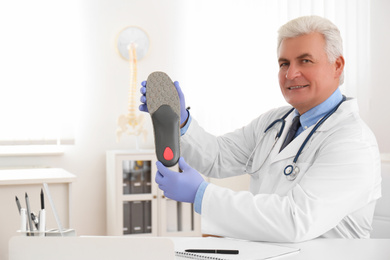 Senior male orthopedist showing insole in clinic