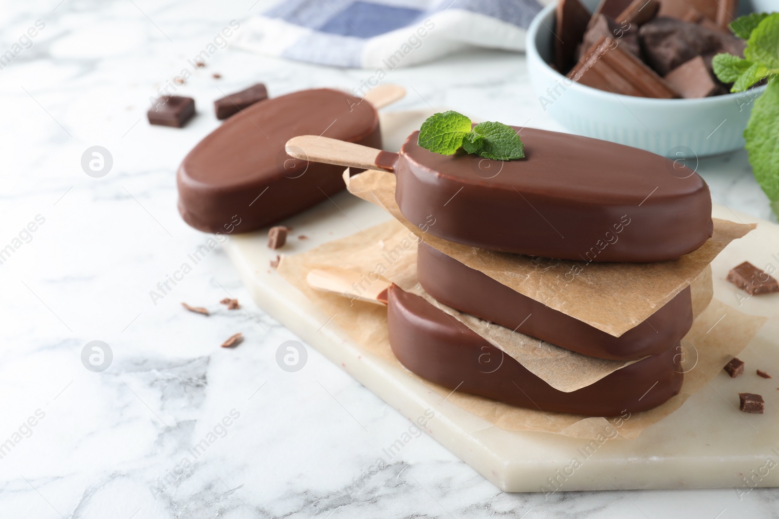 Photo of Delicious glazed ice cream bars with mint on white marble table.  Space for text