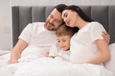 Pregnant woman with her son and husband in bed at home. Cute family