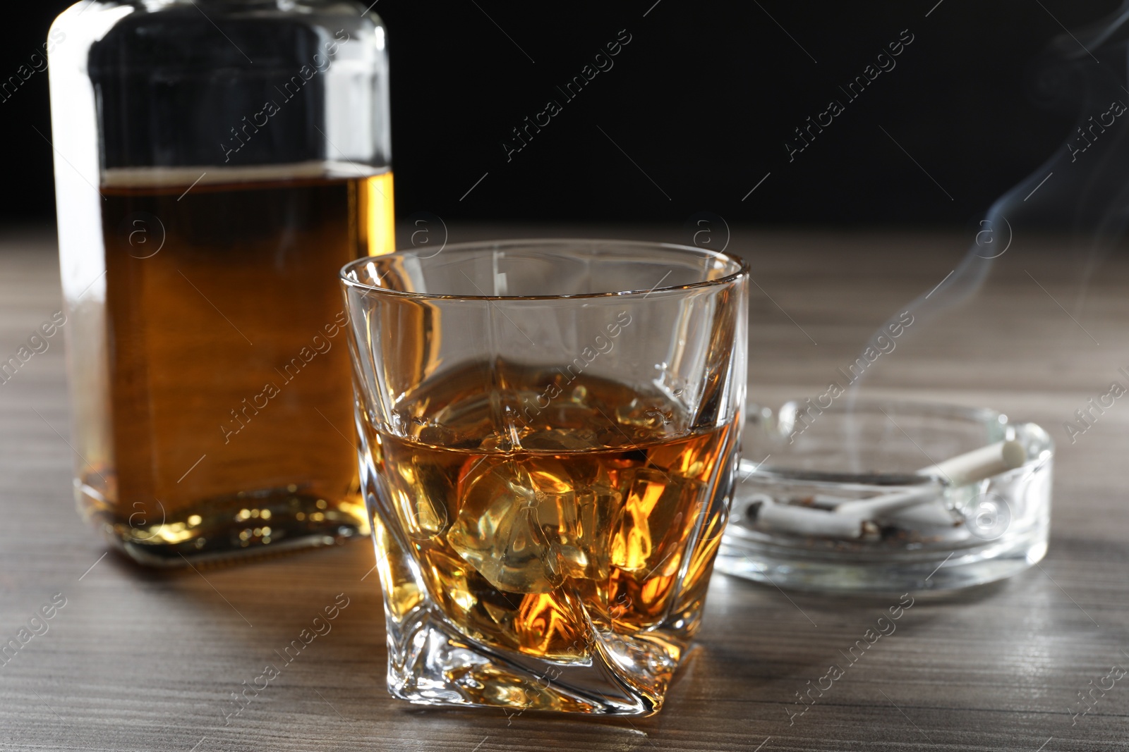 Photo of Alcohol addiction. Whiskey in glass, bottle, cigarettes and ashtray on wooden table