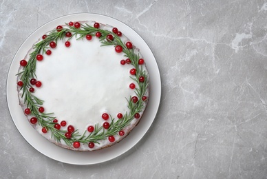 Traditional Christmas cake decorated with rosemary and cranberries on light grey marble table, top view. Space for text