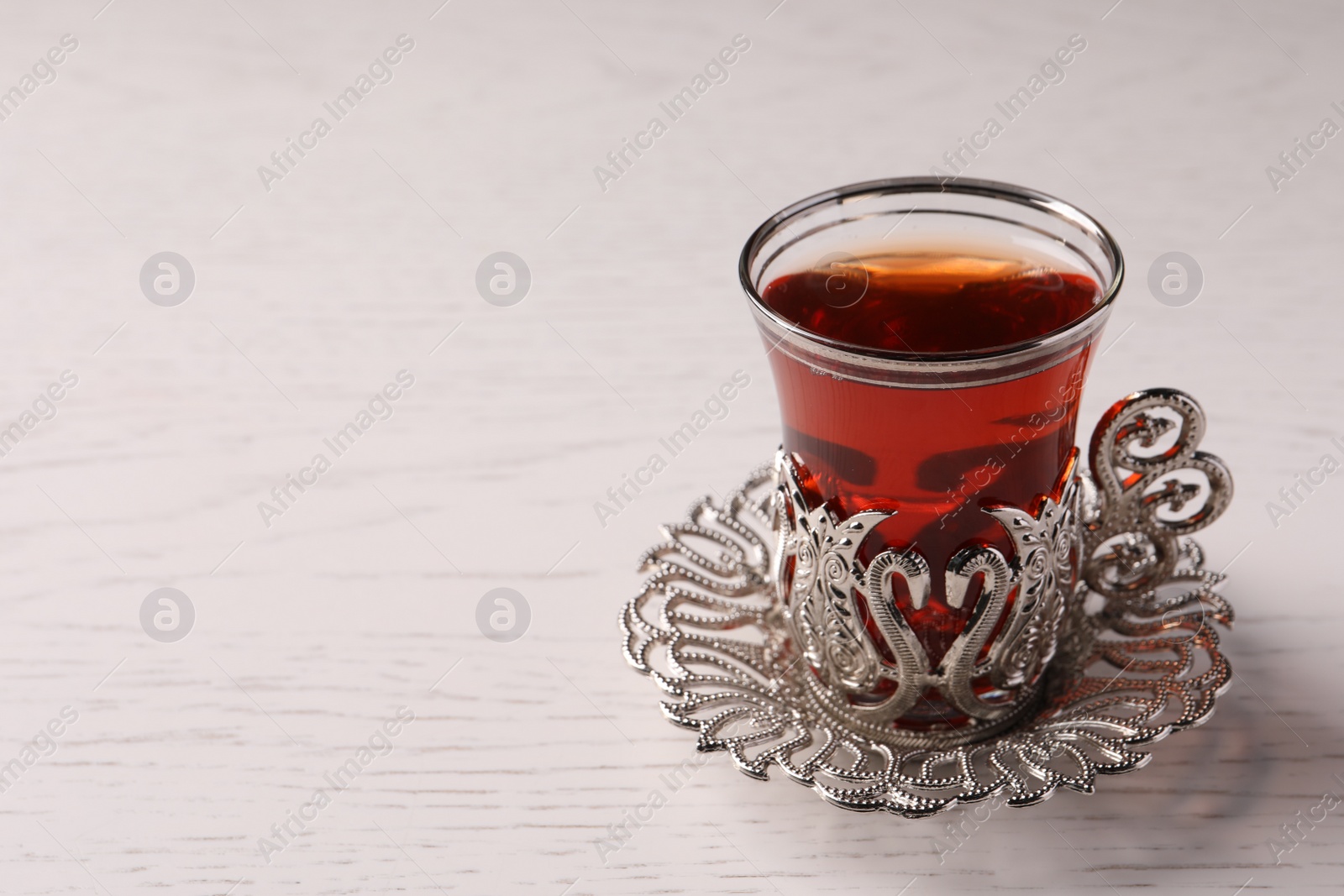 Photo of Glass of traditional Turkish tea in vintage holder on white wooden table, closeup. Space for text