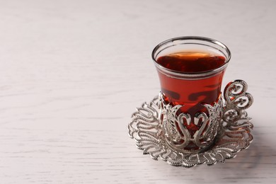 Photo of Glass of traditional Turkish tea in vintage holder on white wooden table, closeup. Space for text