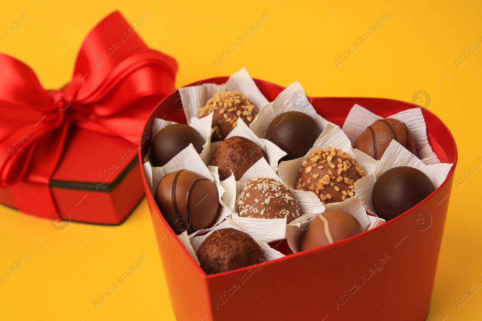 Photo of Heart shaped box with delicious chocolate candies on yellow background, closeup