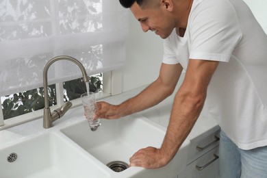Man filling glass with water from tap at home