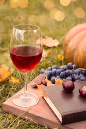 Photo of Glass of wine, book and chestnuts on wooden board outdoors. Autumn picnic