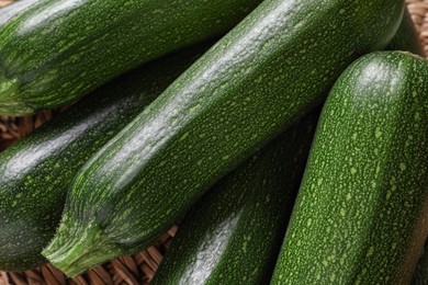 Raw ripe zucchinis on wicker mat, closeup