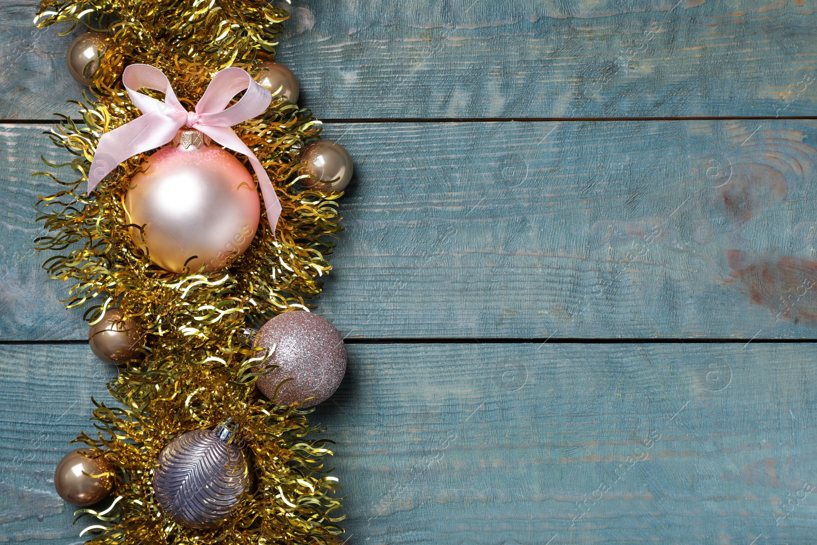 Photo of Bright tinsel and Christmas balls on light blue wooden background, flat lay. Space for text