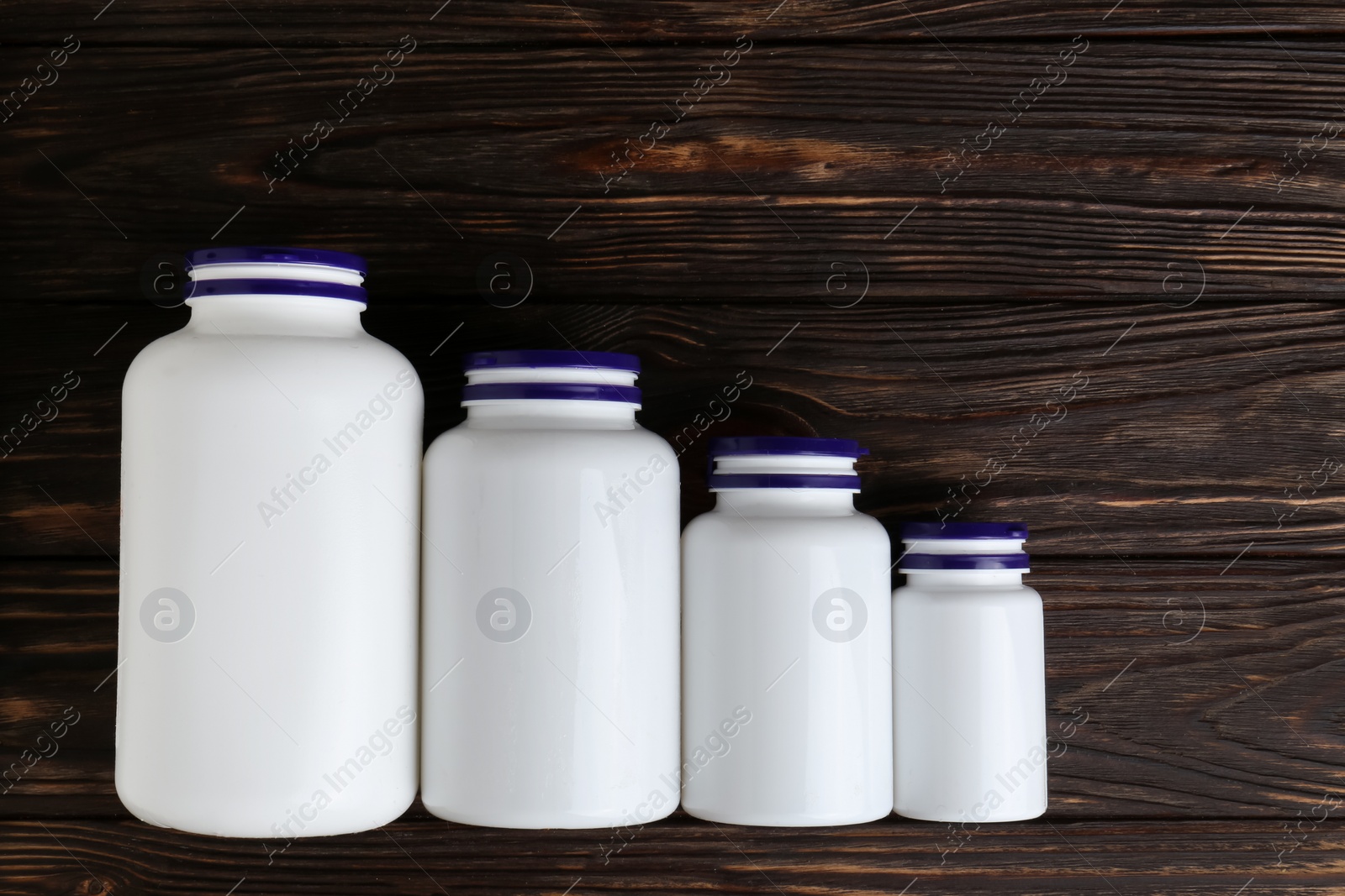 Photo of White medical bottles and pills on wooden table, flat lay