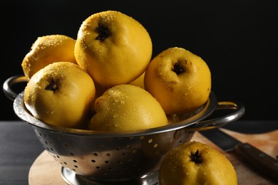 Tasty ripe quinces with water drops in metal colander and knife on black wooden table, closeup