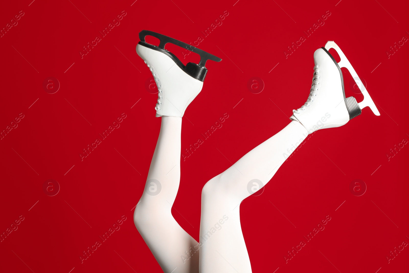 Photo of Woman in elegant white ice skates on red background, closeup of legs