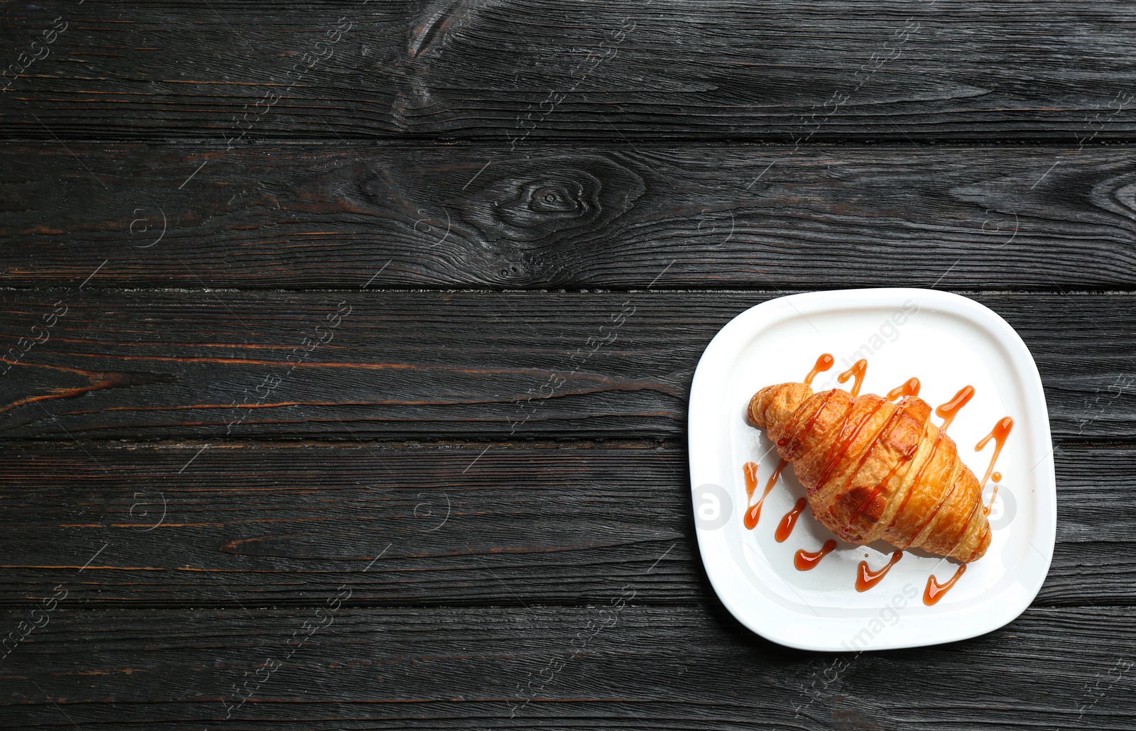 Photo of Plate of tasty croissant with jam and space for text on dark wooden background, top view. French pastry