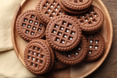 Tasty chocolate sandwich cookies with cream on wooden table, top view