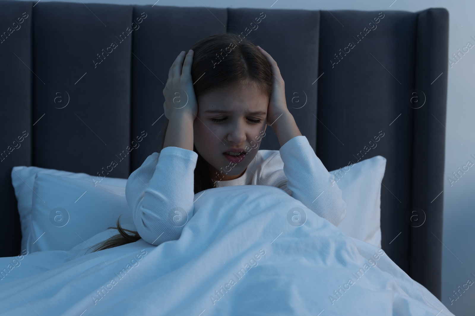 Photo of Little girl suffering from headache in bed at night