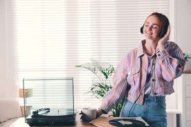 Photo of Young woman drinking coffee while listening to music with turntable at home