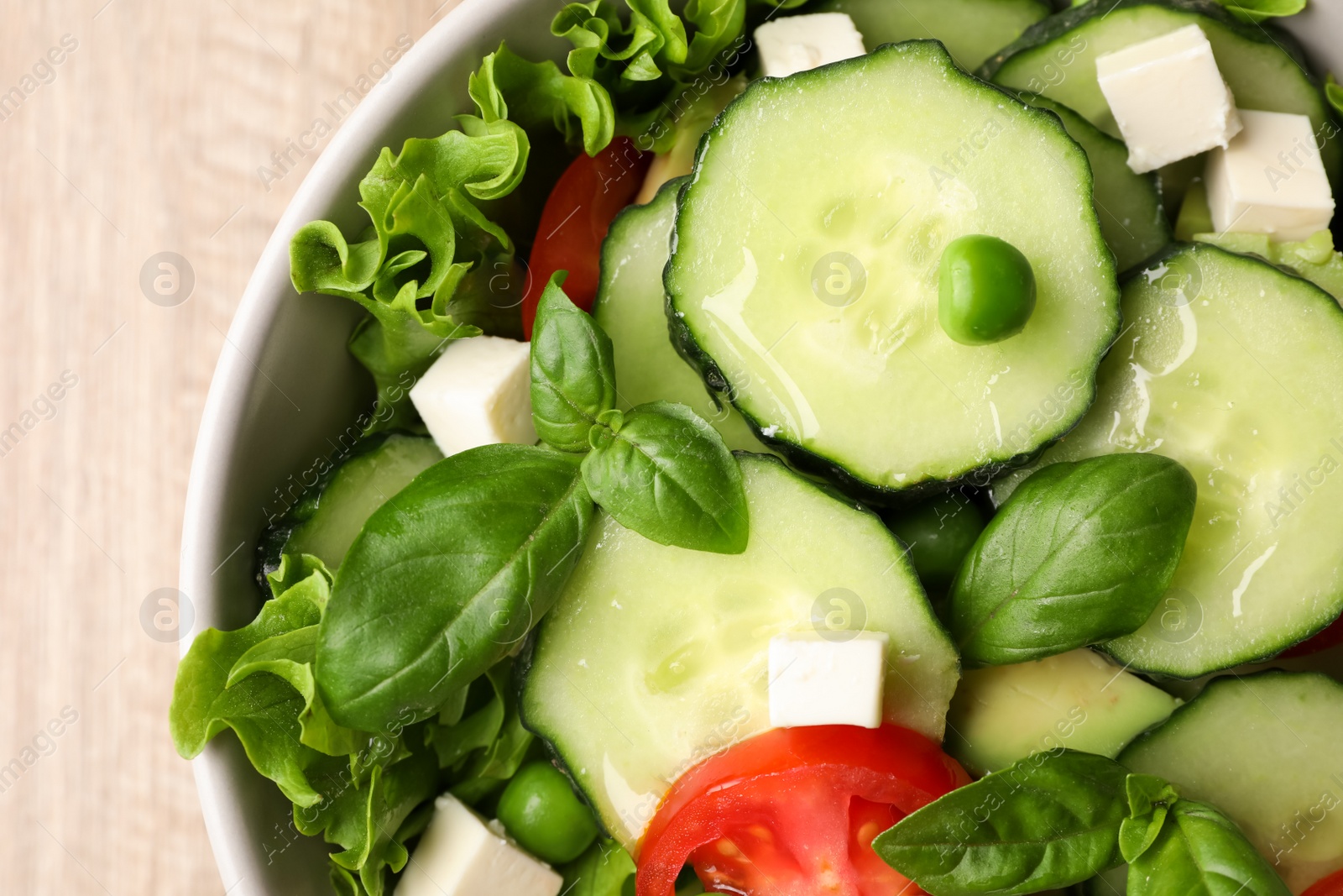 Photo of Tasty fresh salad with cucumber in bowl on table, top view