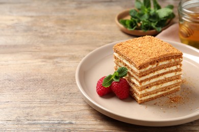 Photo of Slice of delicious layered honey cake served with mint and raspberries on wooden table. Space for text