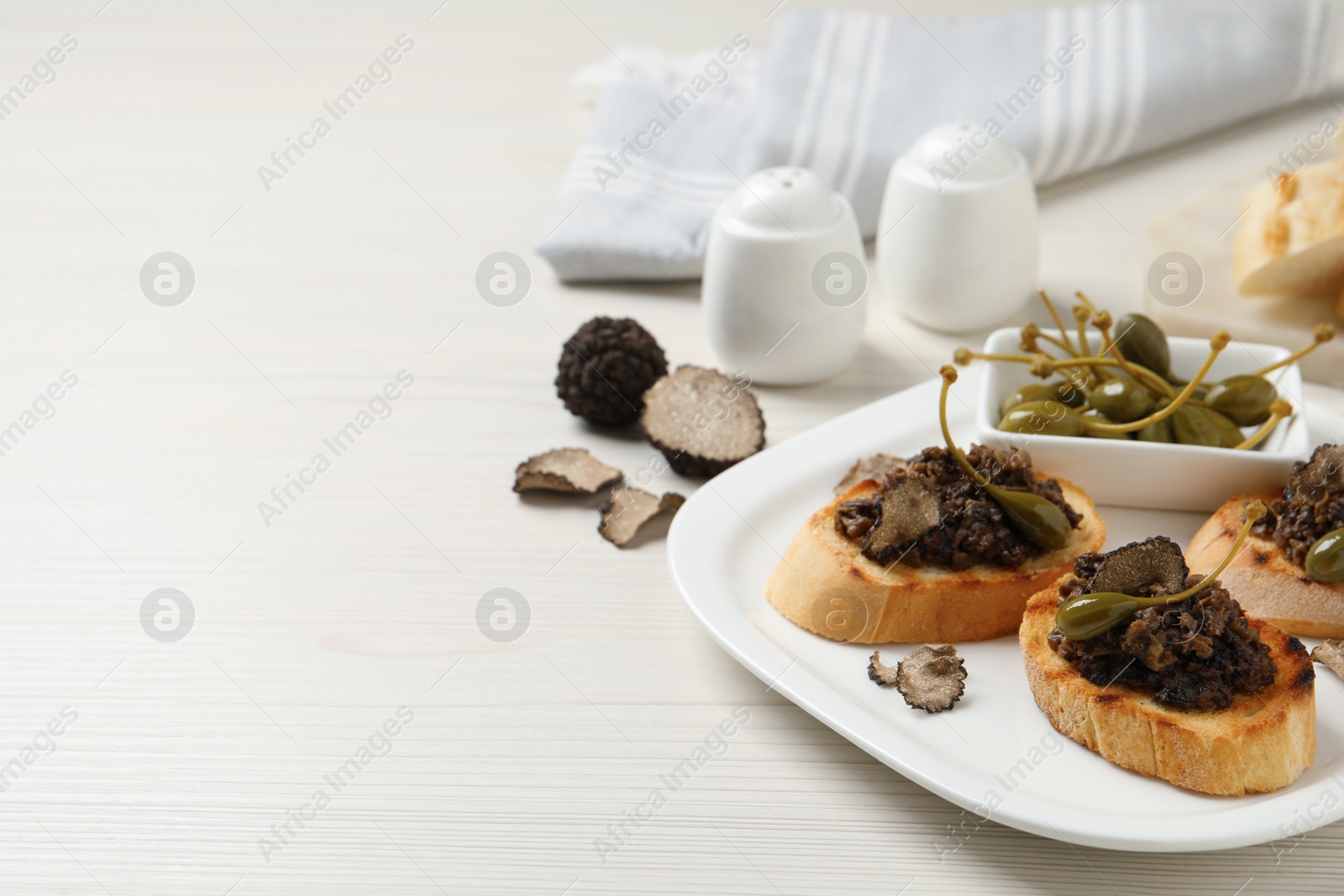 Photo of Delicious bruschettas with truffle sauce and caperberries on white wooden table. Space for text