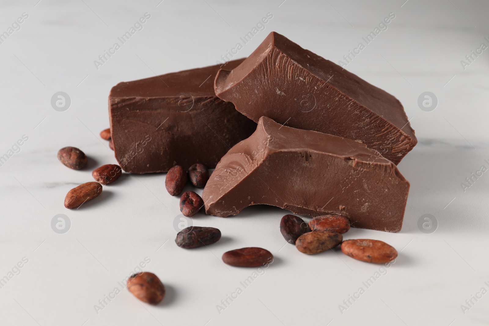 Photo of Pieces of tasty milk chocolate and cocoa beans on white marble table, closeup