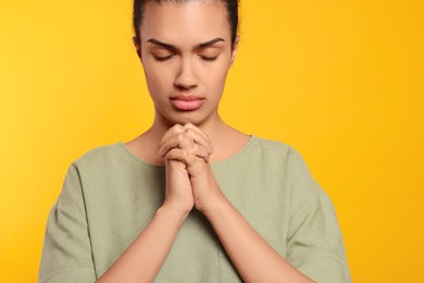 African American woman with clasped hands praying to God on orange background