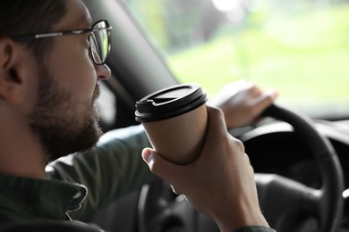 Coffee to go. Man with paper cup of drink driving his car, closeup