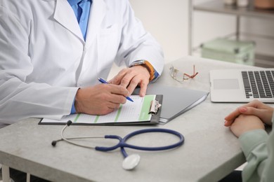 Photo of Doctor filling patient's medical card at table in clinic, closeup
