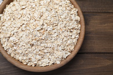 Photo of Raw oatmeal in bowl on wooden table, top view