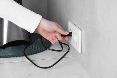 Photo of Woman plugging blender into socket at white table indoors, closeup